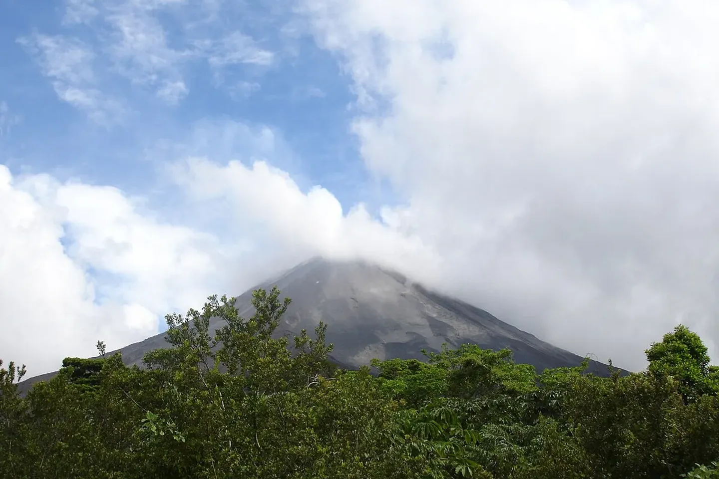 Clouds drift over Arenal Volcano above the green forest canopy.