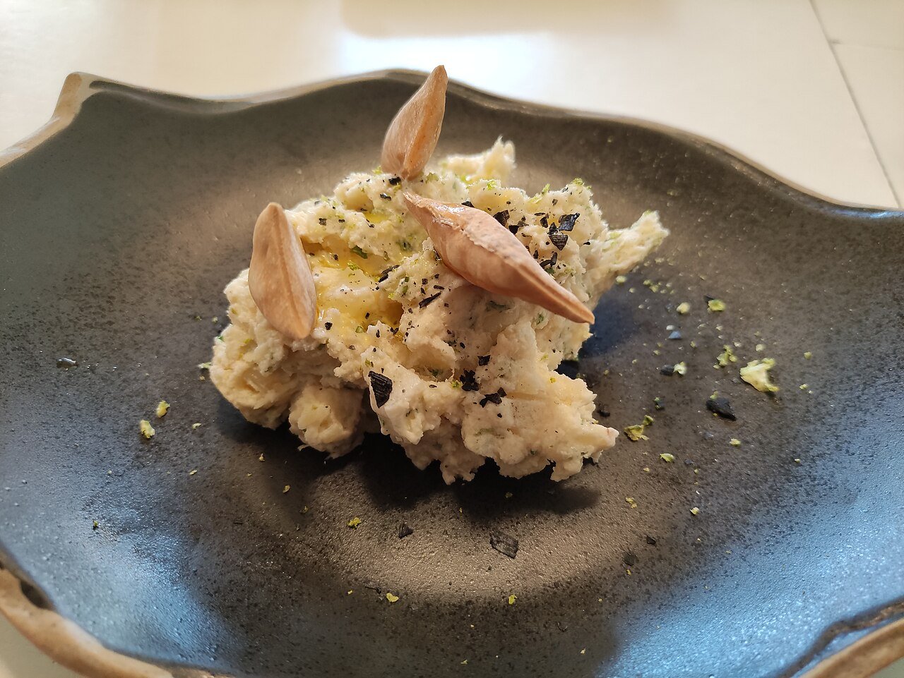 Trinxat — the potato-and-cabbage mash considered Andorra's national dish — plated with squid salad and garnish on a dark ceramic dish