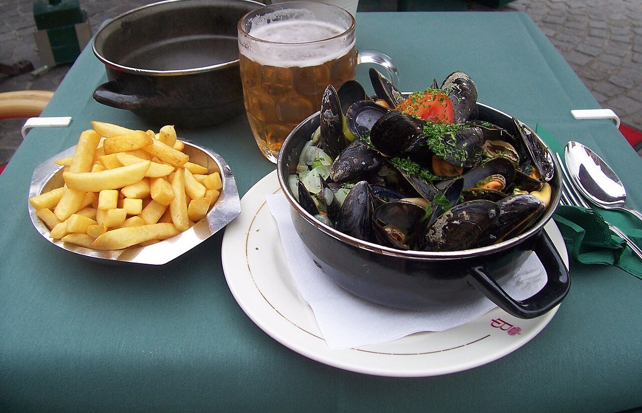 A pot of moules-frites — steamed mussels with fries and a beer — on an outdoor table in Bruges