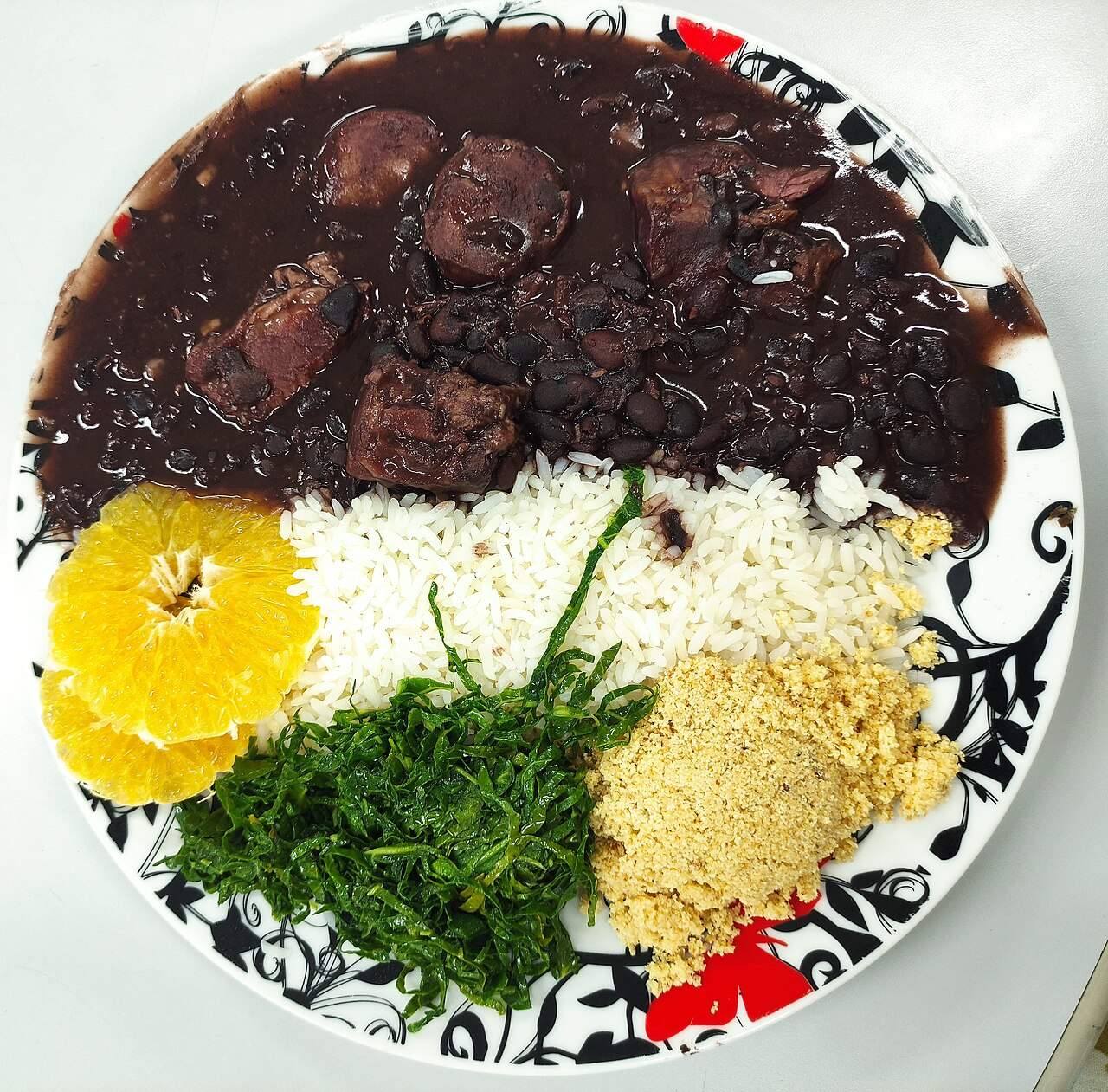 A plate of feijoada carioca — black bean and pork stew with rice, collard greens, farofa and orange slices