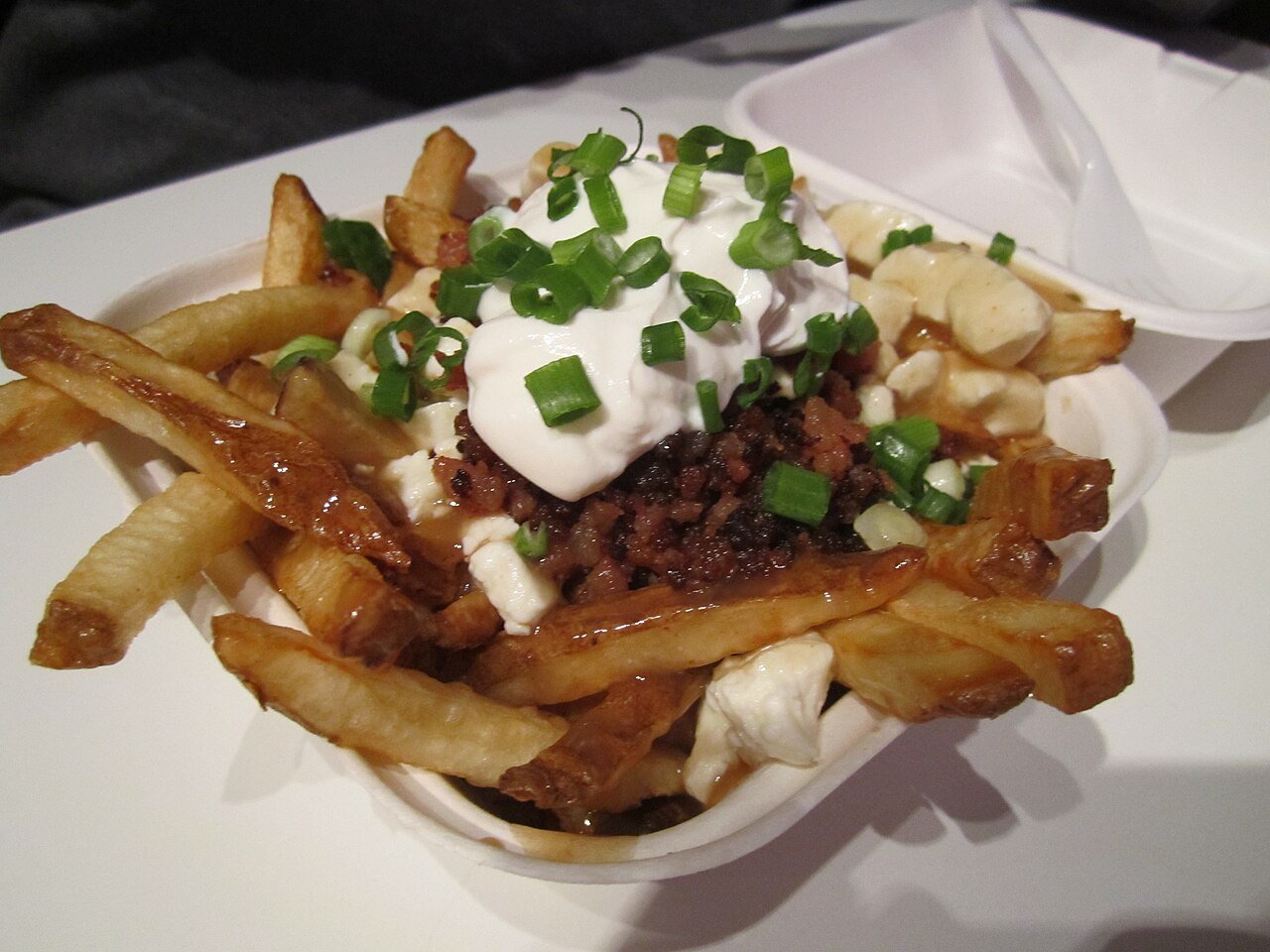 Loaded poutine in a takeout container — French fries with cheese curds, gravy, sour cream and scallions