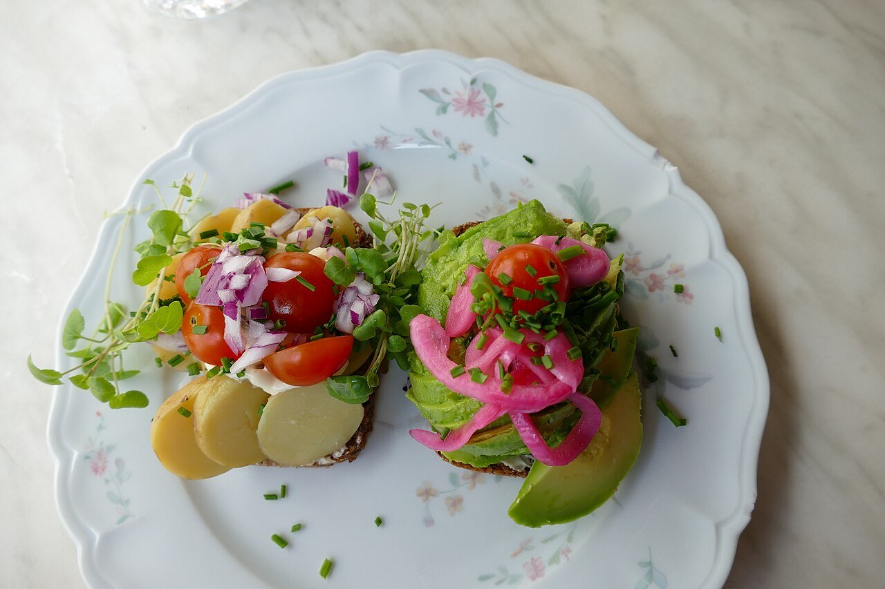 Open-faced smørrebrød sandwiches — one with avocado, one with potatoes — in Copenhagen, Denmark