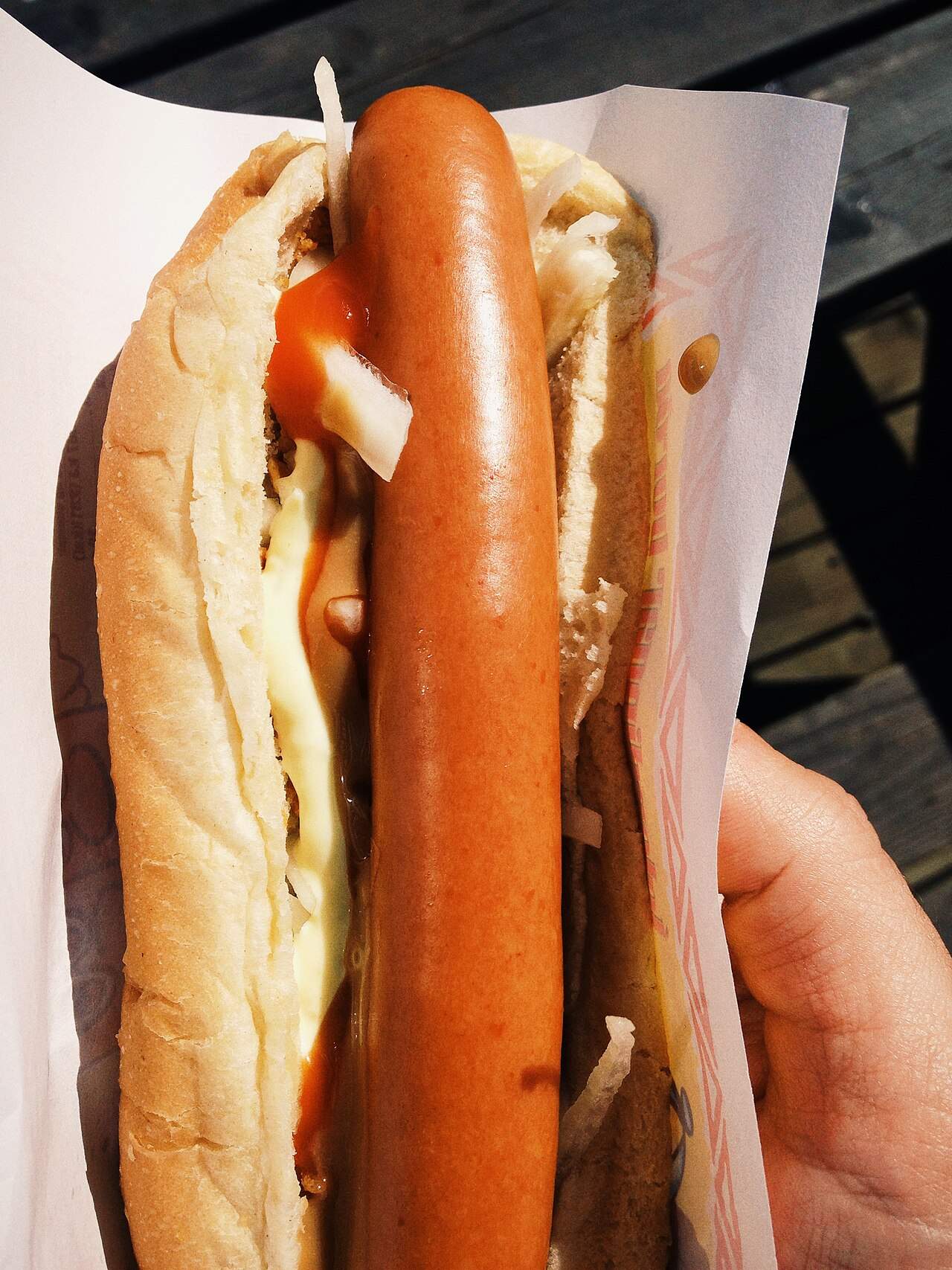A classic Icelandic hot dog loaded with onions and sauces, held in a paper wrapper