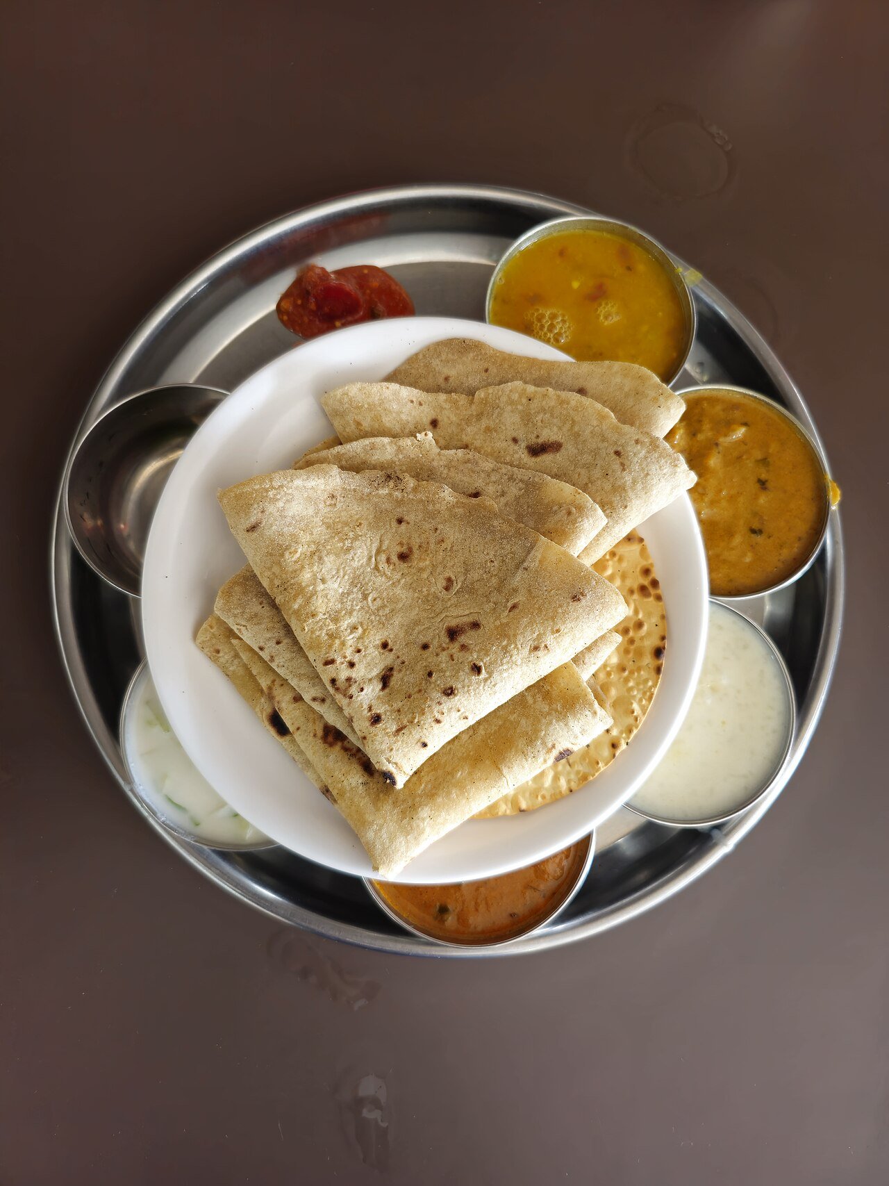 A vegetarian thali with chapatis, curries, and raita on a steel plate in Mumbai, India