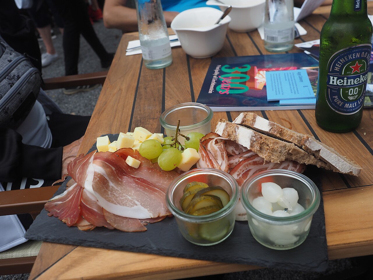 A Liechtenstein-style board of cured bacon, cheese, grapes, gherkins, pickled onions, and bread