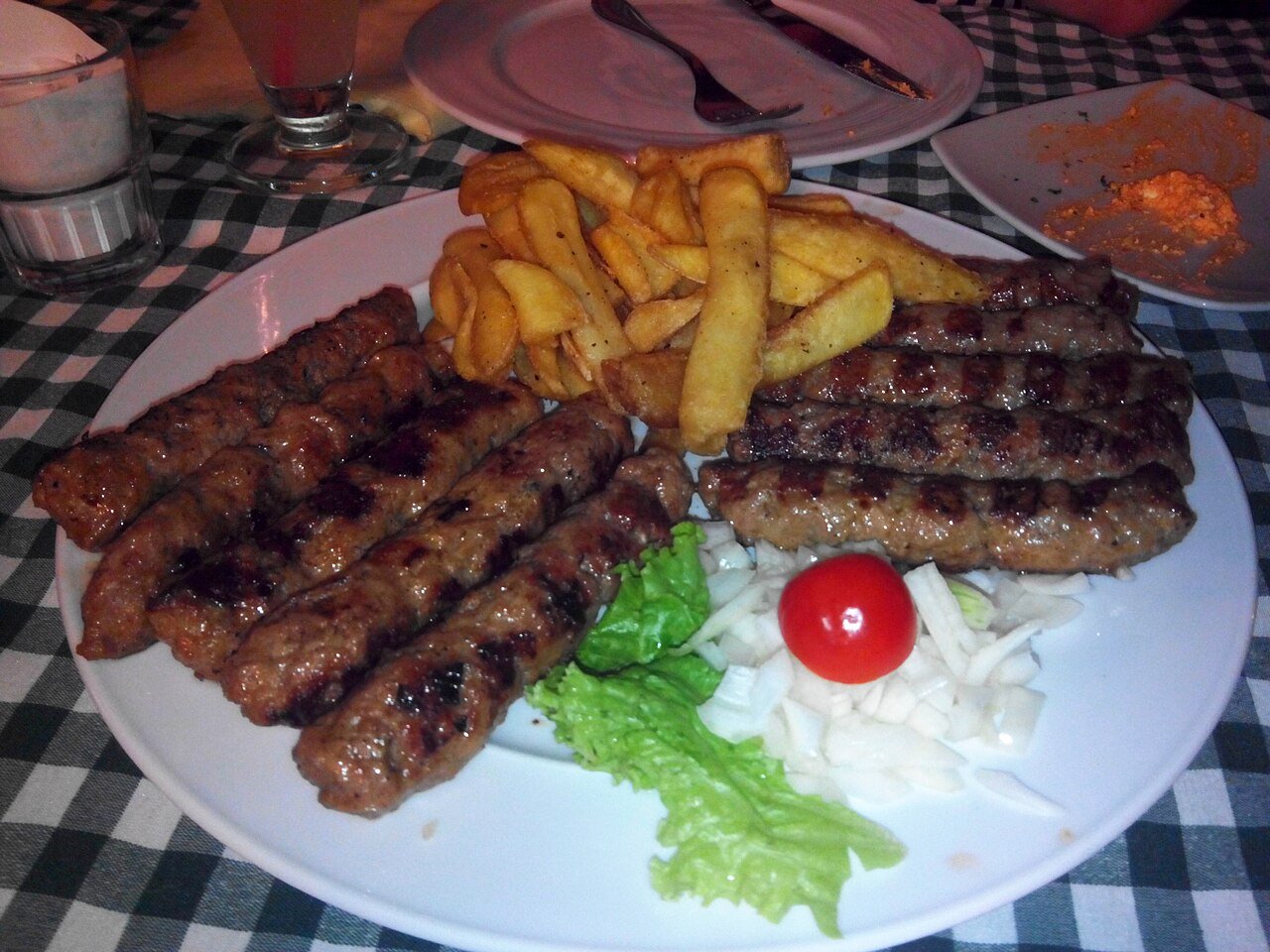 A plate of ćevapi — grilled minced-meat kebabs — with fries, onions and tomato in Budva, Montenegro