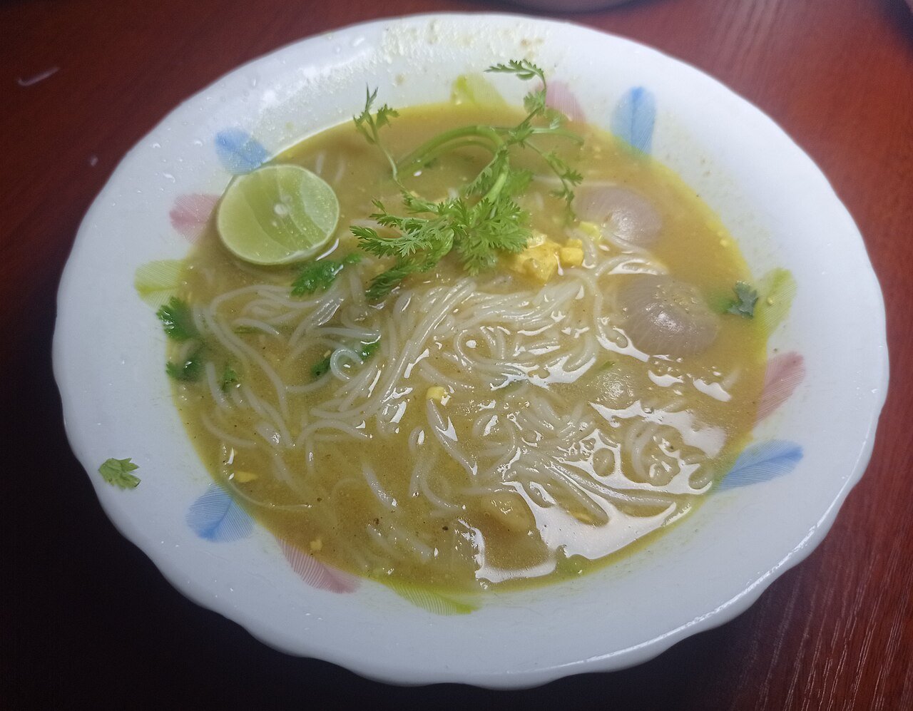 A bowl of mohinga, Myanmar's fish noodle soup, garnished with lime and herbs