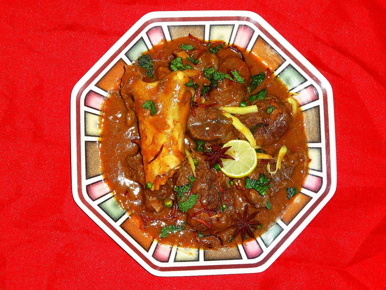 A plate of beef nihari, a slow-cooked beef stew garnished with ginger, mint, and lime