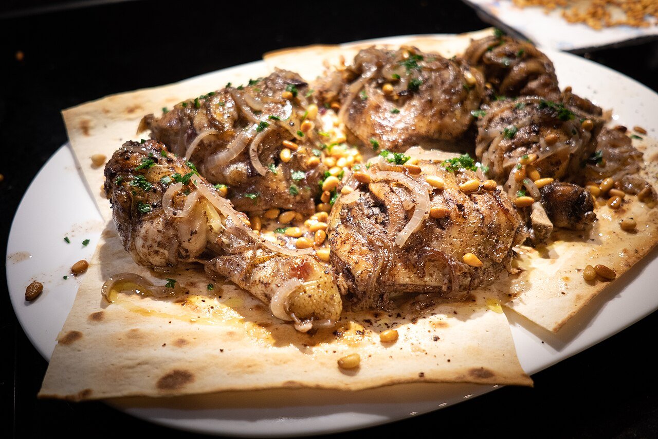 Mussakhan — Palestine's national dish of sumac-spiced roast chicken with caramelized red onions on flatbread, garnished with pine nuts and herbs