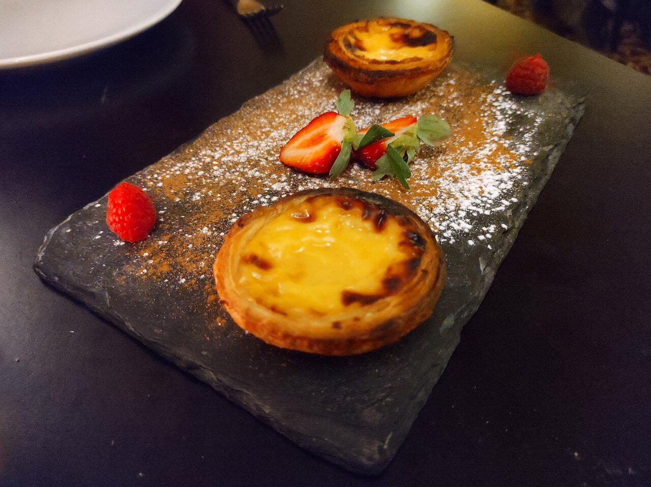 Two pastel de nata custard tarts dusted with cinnamon and plated with berries in Lisbon, Portugal
