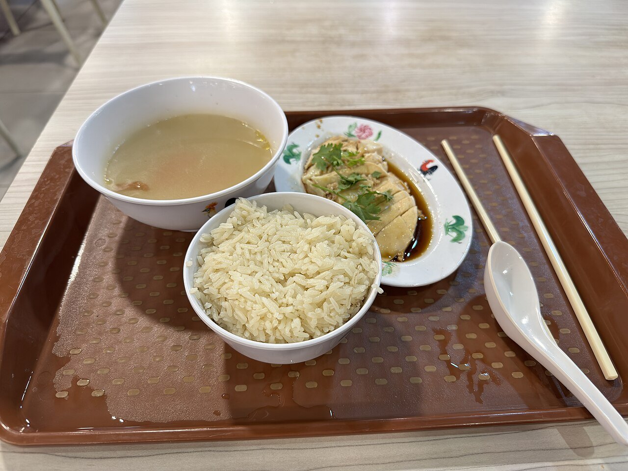 Hainanese chicken rice with chicken broth and seasoned rice on a food court tray in Singapore