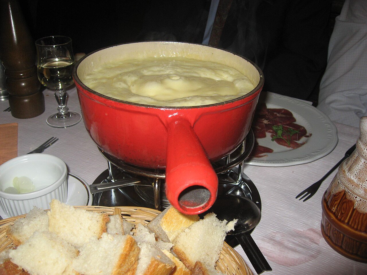 A steaming red pot of Swiss cheese fondue with a basket of bread for dipping, at a restaurant in Geneva