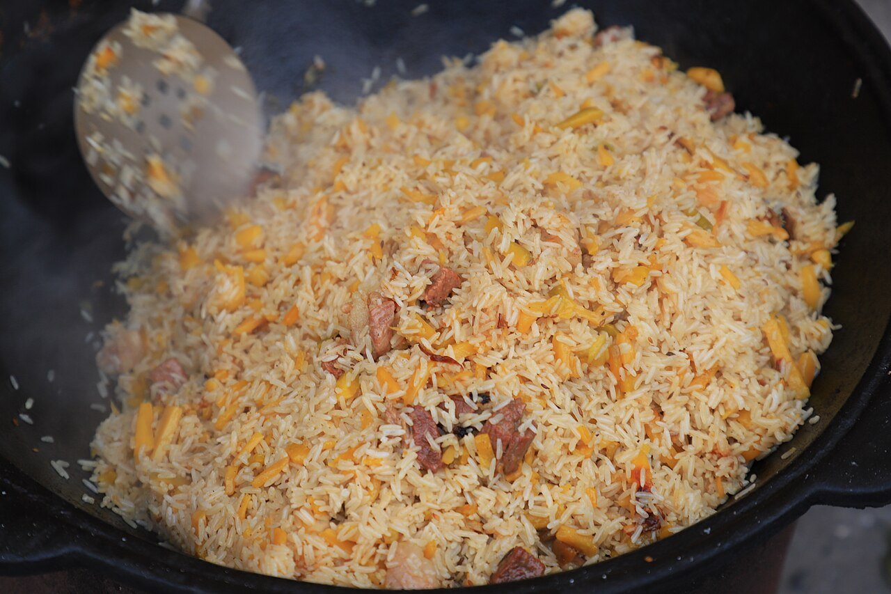 Ferghana-style plov (osh) cooking in a giant cauldron — rice with meat and carrots