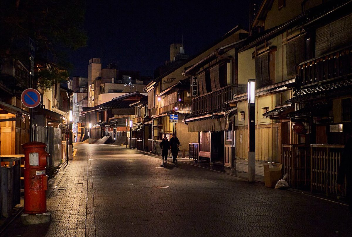 Traditional wooden townhouses and pedestrians on a quiet street in Gion, Kyoto, at night