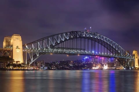 Sydney Harbour Bridge illuminated at night above the water at Circular Quay.